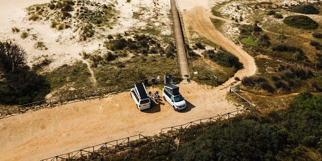 VW California Beach und Ocean auf sandigem Platz an der potugisischen Küste aus Vogelperspektive.