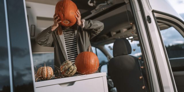 A woman in a CamperBoys van holding a pumpkin and is covering her face with it.