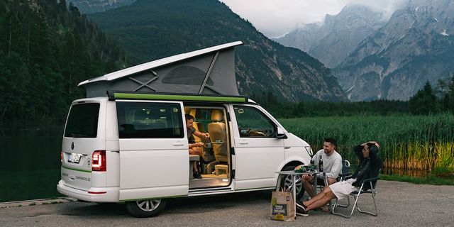 Vor und in einem CamperBoys Camper sitzen Freunde und unterhalten sich. Im Hintergrund sind die Berge zu sehen. 