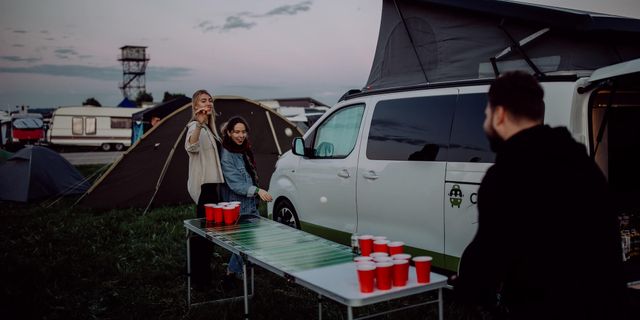 Three friends playing beer pong. In the background is a parked CamperBoys van and a tent.