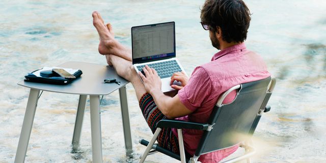Ein Mann hat seinen Campingtisch und -stuhl in einem Fluss aufgebaut und arbeitet an seinem Laptop.