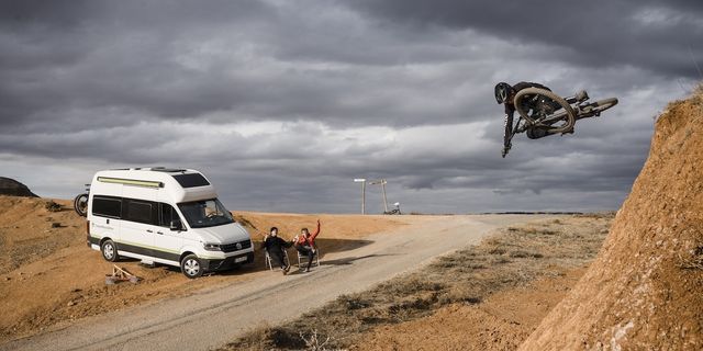 Two people sitting next to a parked CamperBoys van and watching a mountainbiker 