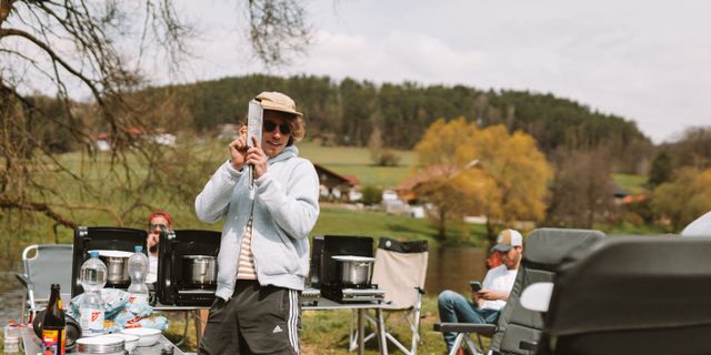 Mann tanzt mit Käsereibe zwischen den Stühlen am Campingplatz.