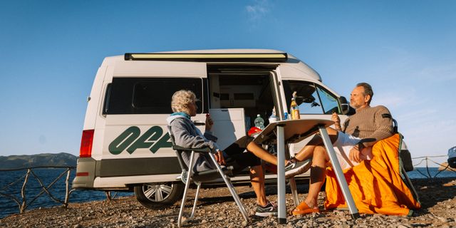 Ein älteres Pärchen frühstückt vor einem Off VW Grand California, im Hintergrund ist das Meer