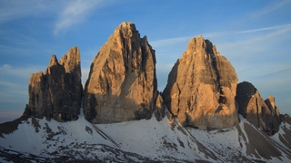 Die Drei Zinnen oder Tre Cime, für die die Dolomiten bekannt sind. Die drei Gipfel werden vor dem blauen Himmel von der Sonne angestrahlt.