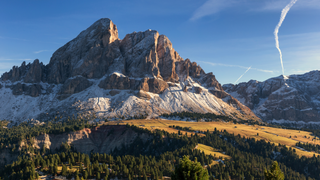 Das Würzjoch als Dolomiten Urlaub Tipp: Der imposante Gipfel des Würzjochs in Italien, vor dem sich Almwiesen erstrecken, angestrahlt von der Sonne.