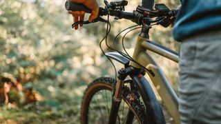 Nahaufnahme des vorderen Teils eines grünen Mountainbikes auf einem Waldweg, dessen Bremse gerade gedrückt wird