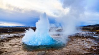 Der Golden Circle auf der Island Rundreise: Ein sprudelnder und dampfender Geysir in karger Landschaft auf Island