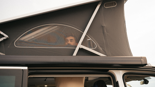 Ein junger Mann schaut beim Aufbauen seines Camper Aufstelldachs aus dem Fenster nach draußen.