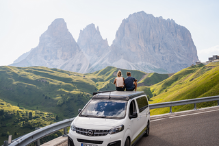 Zwei Personen sitzen auf Camper und schauen in die Berge