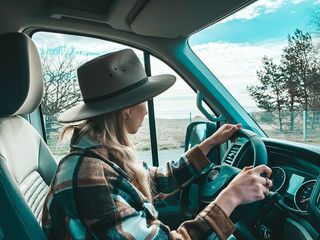 Frau mit Hut und Karohemd sitzt am Lenkrad eines VW California Ocean.