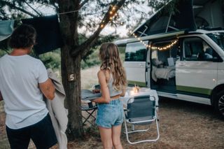 Ein Vater hängt mit seiner Tochter die Wäsche an der Wäscheleine neben ihrem Camper mit Aufstelldach auf.