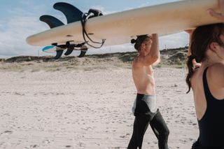 Zwei Personen mit Surfbrett auf dem Kopf in Frankreich an der Atlantikküste