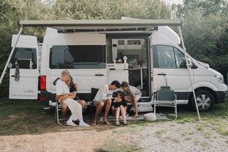 Familie mit Kindern sitzt auf Campingplatz vor ihrem Camper