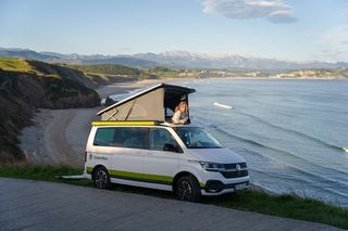 Eine Frau blickt aus dem Dachzelt eines Campers aufs Meer.