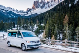 Ein CamperBoys Van fährt eine Straße in einem verschneiten Gebirge entlang.