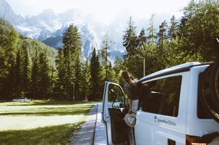 Eine Frau lehnt sich aus einem geparkten Camper heraus und betrachtet eine Bergkulisse.