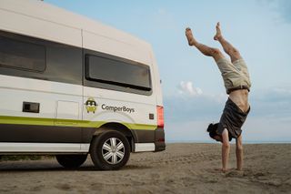 Ein Mann macht vor einem VW Camper einen Handstand.