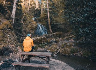 Ein Mann sitzt auf einer Picknickbank und sieht einen Wasserfall an.