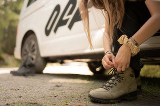 Eine Frau sitzt in der offenen Schiebetür eines Off Campers und bindet sich die Wanderschuhe. Lies hier alles zu Camping Bannwaldsee.