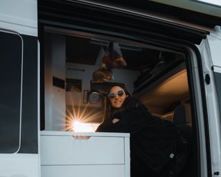 Woman with sunglasses looks out of her camper in Holland at sunset