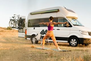 Woman doing yoga in colorful clothes in front of her off camper