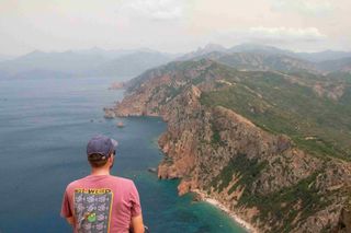 Man with colorful shirt looking at the sea and mountains on the coast in Corsica