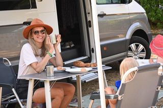 Mutter und Kinder beim Frühstück am Campingtisch vor VW Grand California