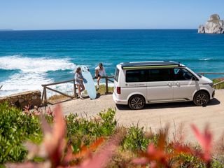 Zwei Freundinnen unterwegs mit dem VW T6.1 California Ocean an der portugiesischen Küste beim Surfen.