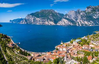 Blick von oben auf den Gardasee mit Ortschaft auf der einen Seite und Berglandschaft auf der anderen.