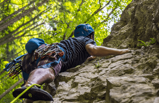 Mann in Kletterausrüstung klettert eine steile Felswand empor.