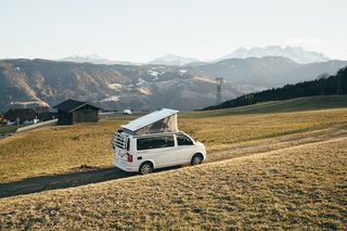 VW California Beach steht in Berglandschaft mit aufgestelltem Dachzelt.