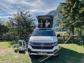 Zwei Frauen sitzen lachend oben im Dachzelt des VW California Ocean.