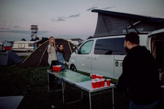 Menschen am Festival spielen vor einem Camper Bierpong.