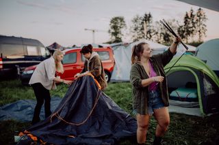 Drei Frauen beim Zeltaufbau auf einem Festivalgelände. Alles, was du fürs Festival Camping brauchst, findest du auf unserer Festival Packliste.