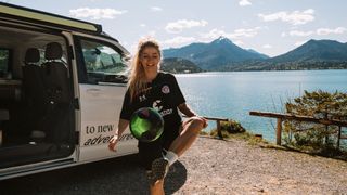 Eine junge Frau spielt während der EM 2024 neben ihrem Camper am Ufer des Walchensees Fußball und lacht dabei