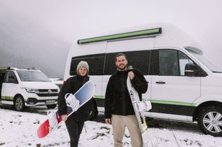 Zwei Personen mit Snowboard in der Hand vor Off Camper im Schnee