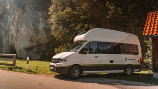 VW Grand California steht im warmen Abendlicht vor einer steilen Bergkante.