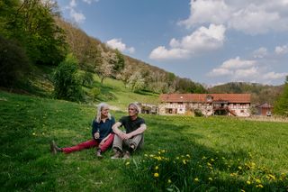 Zwei Menschen sitzen mit Weingläsern auf einer Wiese.