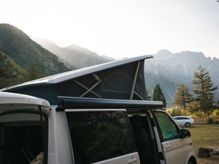 Campingplätze Dolomiten: Ein Camper mit aufgeklapptem Aufstelldach steht vor einer Bergkulisse in der Sonne