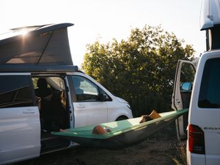 Stromanschluss Campingplatz: Ein Mann liegt in einer grünen, zwischen zwei Campern aufgespannten Hängematte.