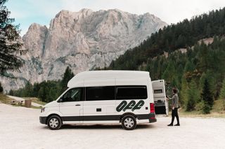 Ein VW Grand California Camper steht auf einer Straße mit Bergen im Hintergrund.