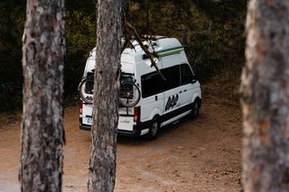 Weißer Off Camper hinter Bäumen auf einem Campingplatz