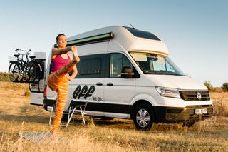 Eine Frau macht vor einem VW Grand California Camper Sport.