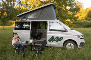 Frau sitzt vor vanexxt Campervan in einer Wiese