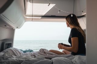 Frau liest Buch in Campervan mit Aussicht auf See