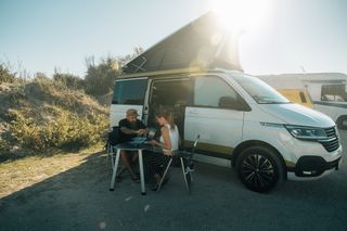 Ein Mann und eine Frau sitzen an einer Campinggarnitur vor einem Camper.