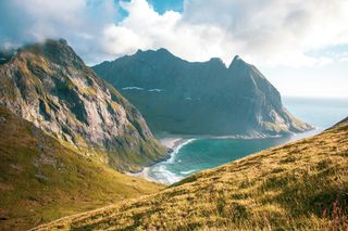 Die Lofoten in Norwegen von oben, man sieht hohe Berge und einen Strand und blaues Meer. Schöne Orte in Norwegen findest du in diesem Artikel.