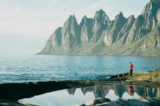 Senja in Norwegen, ein Mann steht an der Küste, man sieht Berge und Meer. In diesem Artikel stellen wir dir schöne Orte in Norwegen vor.