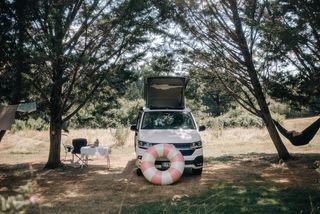 Ein VW California Ocean steht beim Überwintern in Portugal auf einer Wiese. Daneben ist eine Hängematte aufgespannt, ein Schwimmring lehnt am Camper.